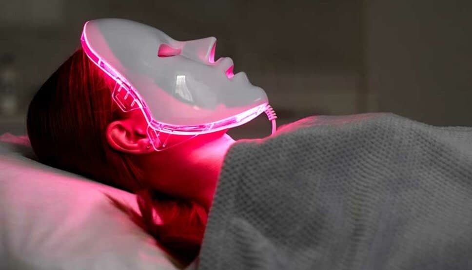 LED light therapy facial mask glowing pink on gray fabric